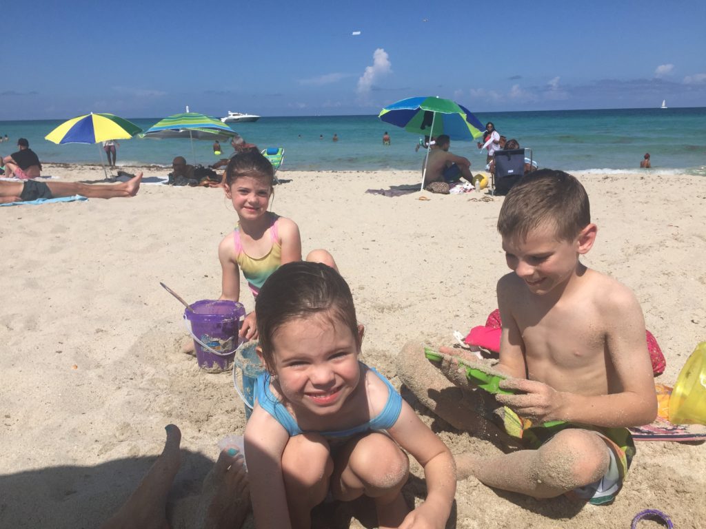 3 kids play on Miami beach with the buckets in the sand.