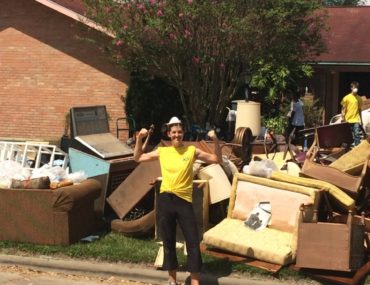 woman flexes muscles in front of a pile of debris dragged out of a home Flooded by Hurricane Harvey in Houston