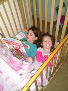 big sister reading to little sister in a crib teaching her to read