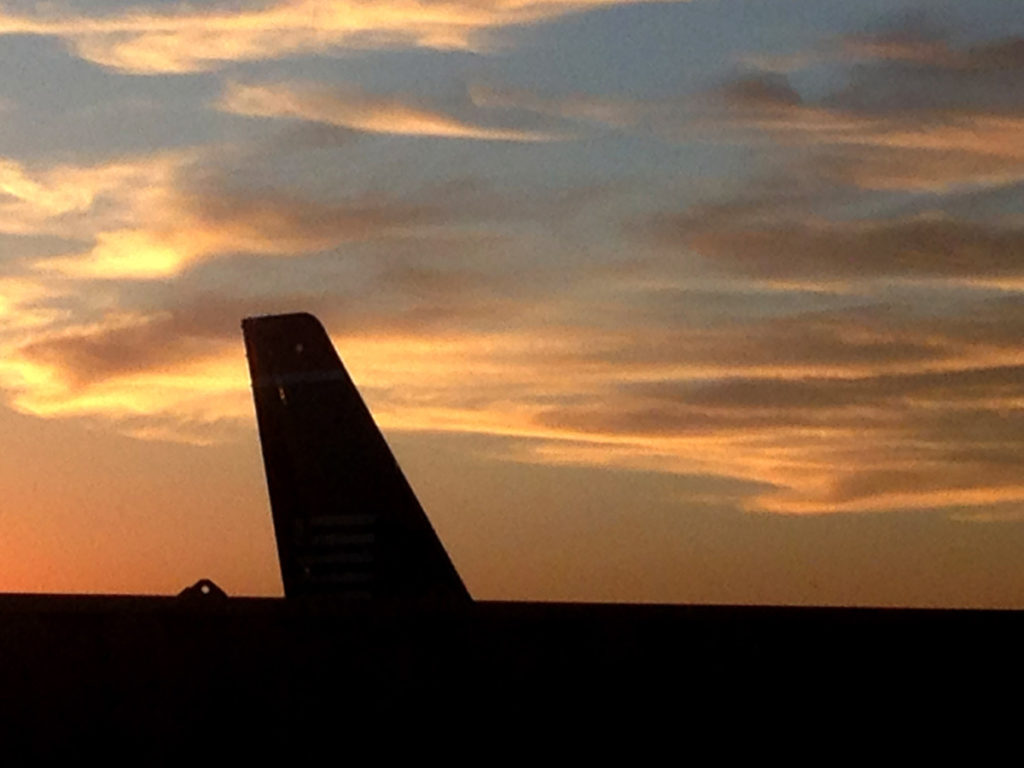 airplane tail in a yellow sunset with wispy clouds