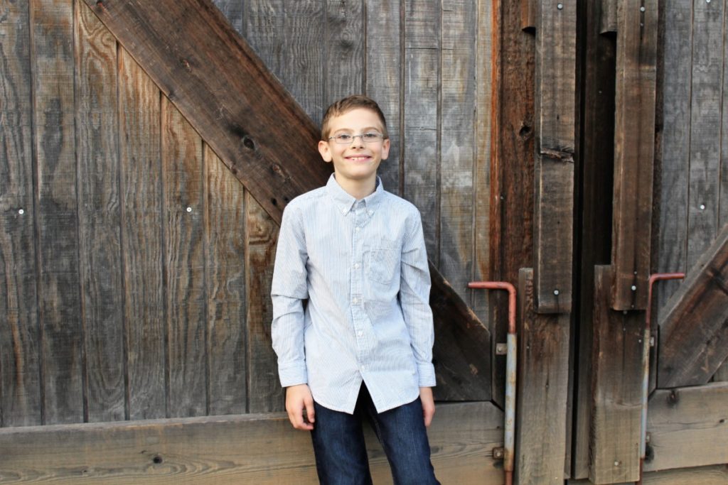 A young boy standing a wooden gate