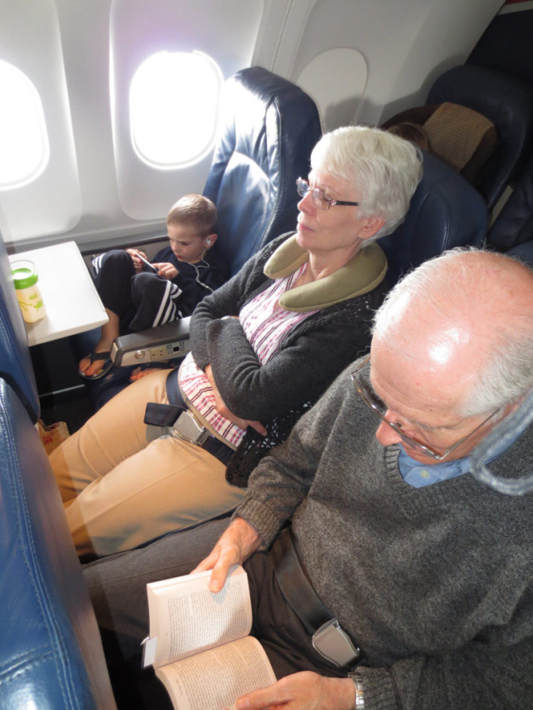 a Boy flys alone while an older couple sleeps and reads next to him