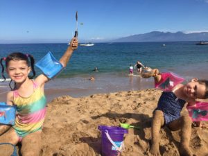 2 young girls playing in the sand at ka'aplalua beach on Maui, Hawaii, molokai in the background