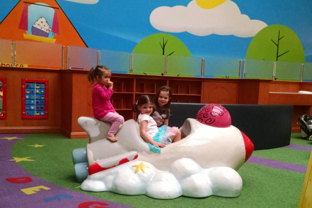 3 little girls play on an airplane at a playplace