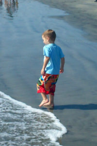 a young boy watches the waves come in and touch his toes
