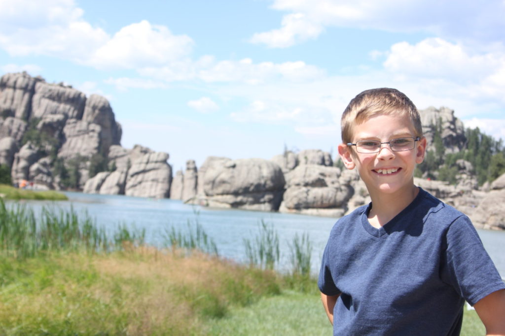 a boy stand in front of Sylvan lake and large boulders in Black Hills, South Dakota 