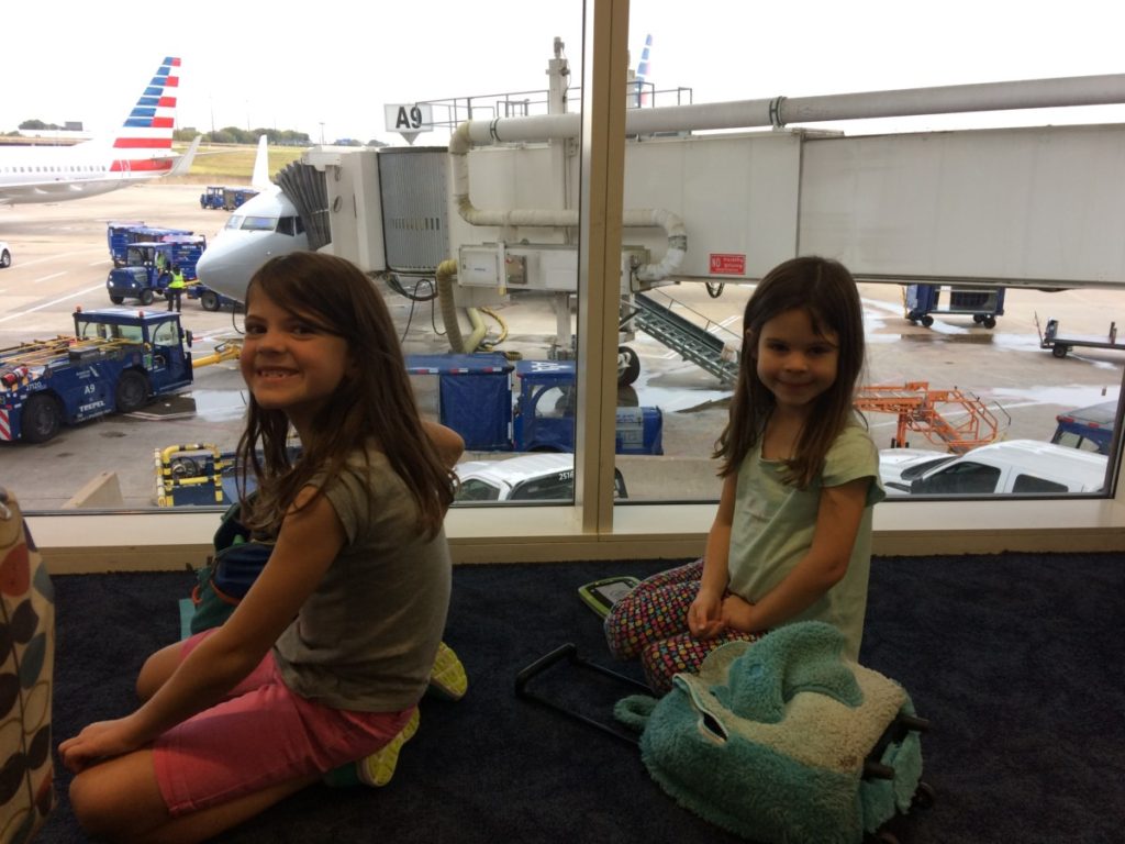 2 girls smile while waiting for a standby flight american airlines airplane in the background
