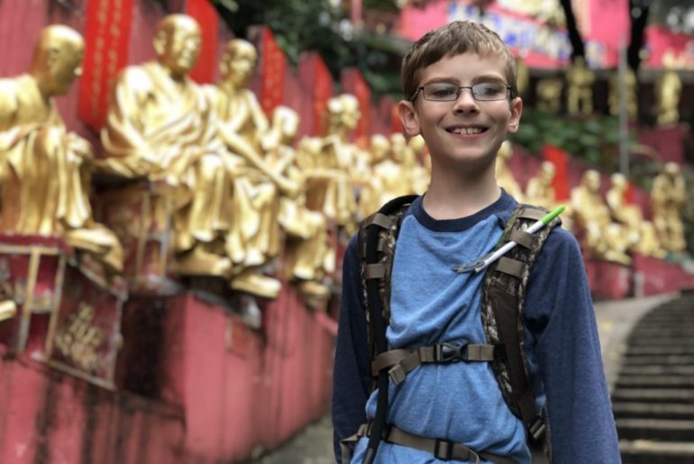Young Boy stands on a path with golden buddha statues in the background