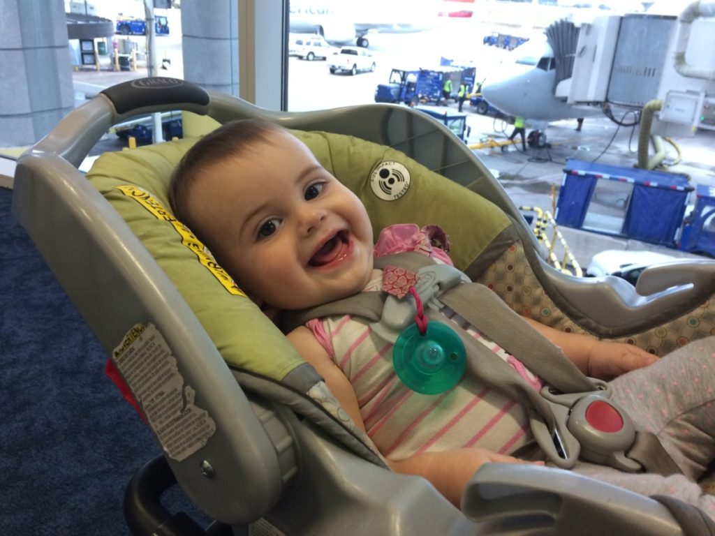 Baby smiles from her carseat with an airplane in the background