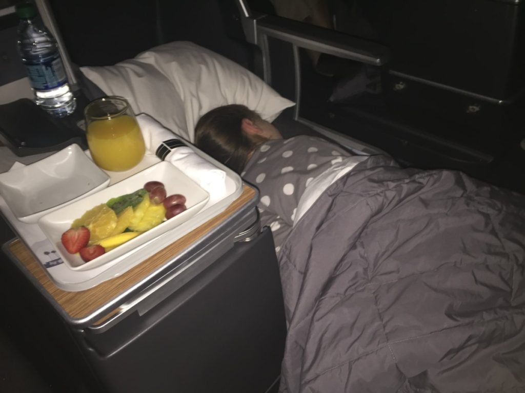 a 6 year old girl sleeps in first class on American Airlines with a first class breakfast waiting for her.
