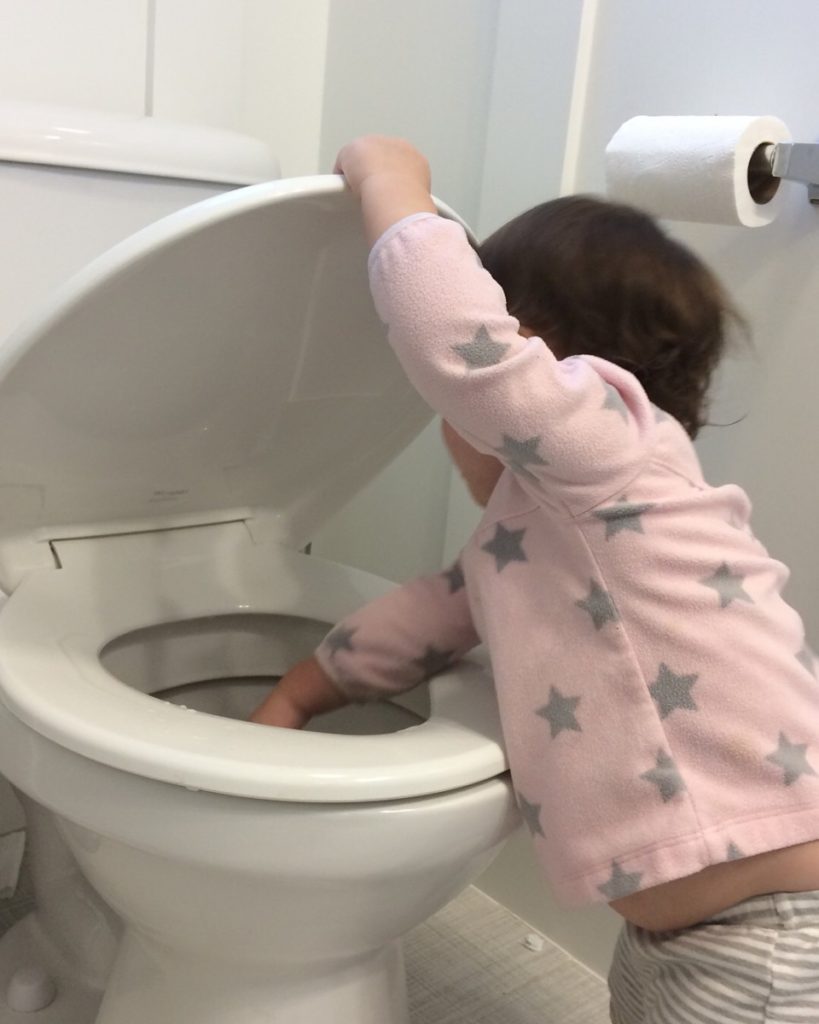 A toddler reaches inside a toilet bowl
