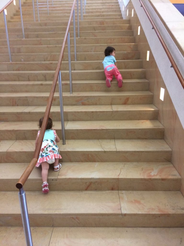 Two toddlers climb museum stairs