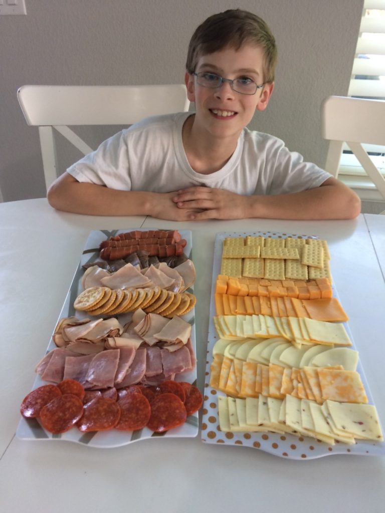 a Boy smiles behind a platter of meats and cheeses he arranged