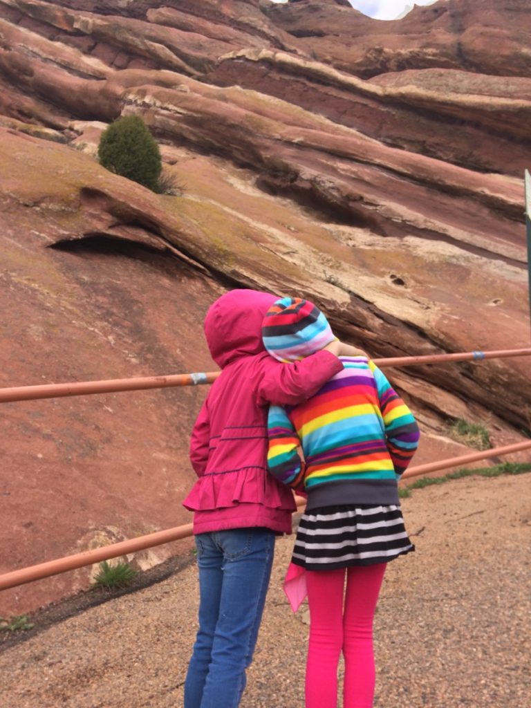 2 girl cousins hug while looking over the massive Red Rocks