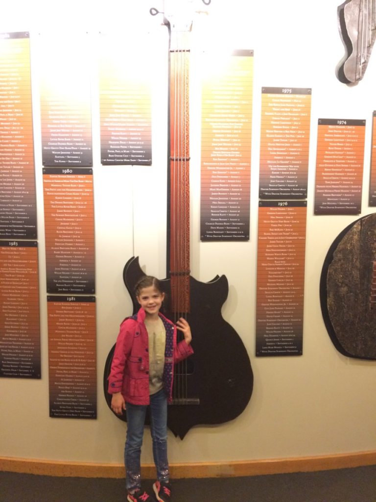 Young girls stands in front of a guitar at Colorado Music Hall of Fame in Red Rocks, Colorado