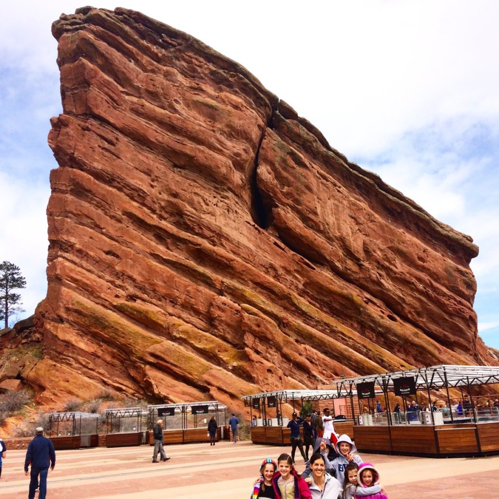 Family poses in front of Massive REd Rock formation at Red Rock Natural Amphitheater.