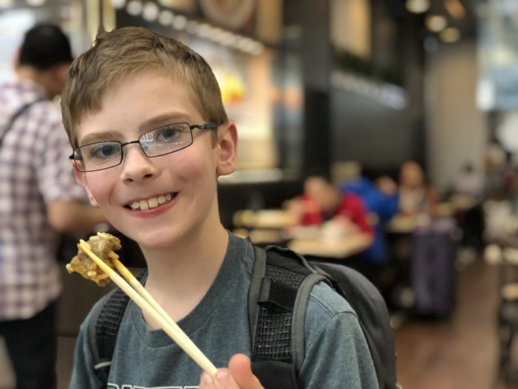 a young American boy eats chicken with chopsticks