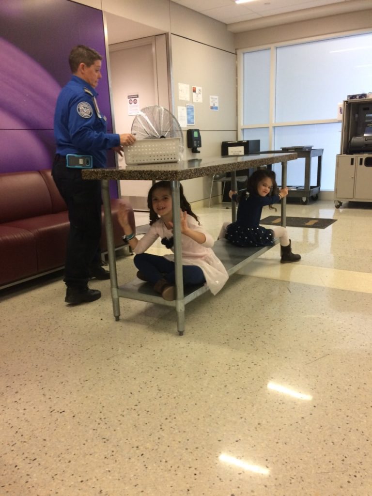 2 girls play under a table at TSA security checkpoint