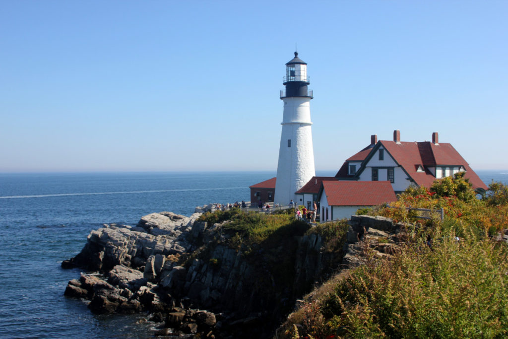 a white lighthouse overlooks a rocky cliff in Portland Maine
