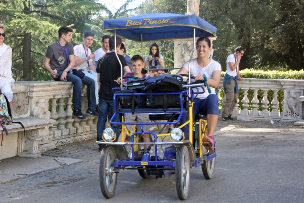 Mom and son ride a bike buggy through Villa Borghese Park in Rome, Italy