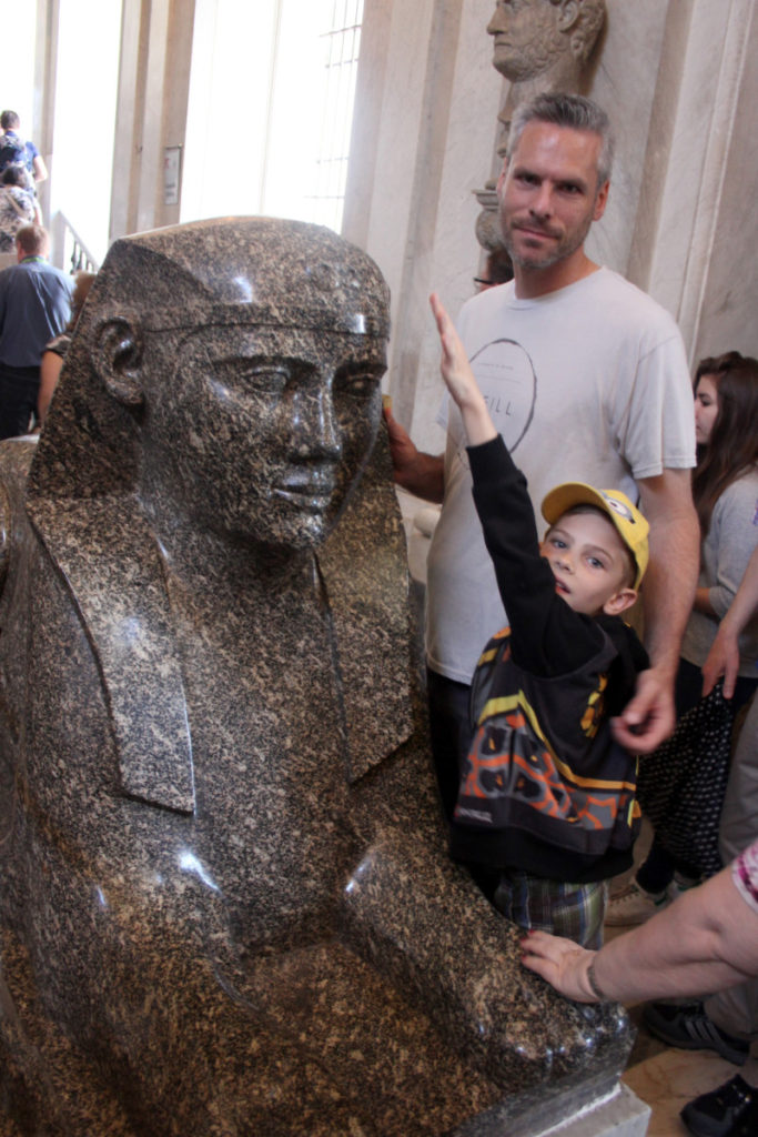 a boy touches an egyptian sculpture in the Vatican Museum