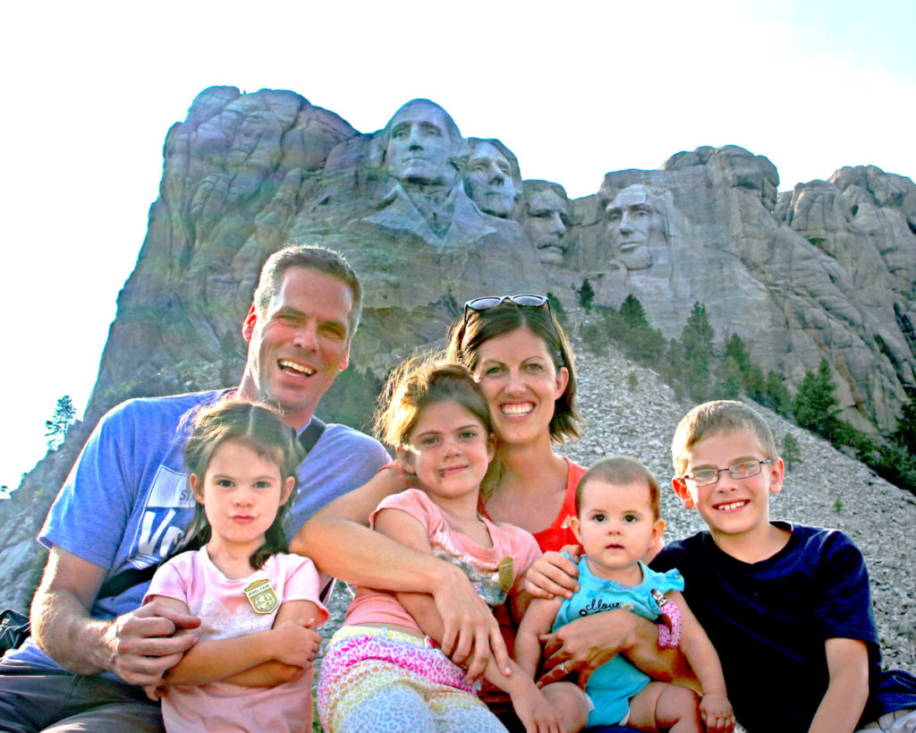 family of 6 pose beneath Mount Rushmore