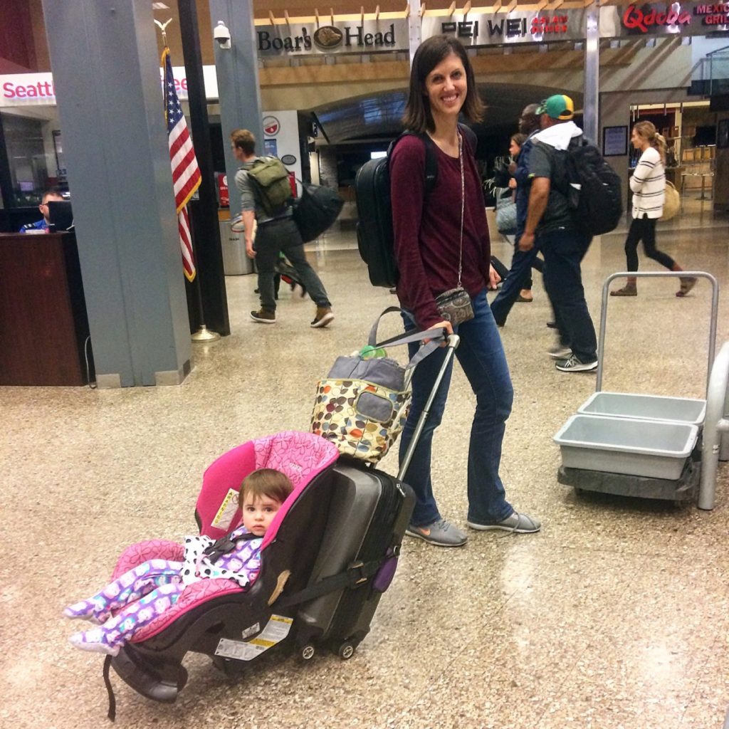 a baby sits in a car seat attached to a carryon as mom pulls her through the airport