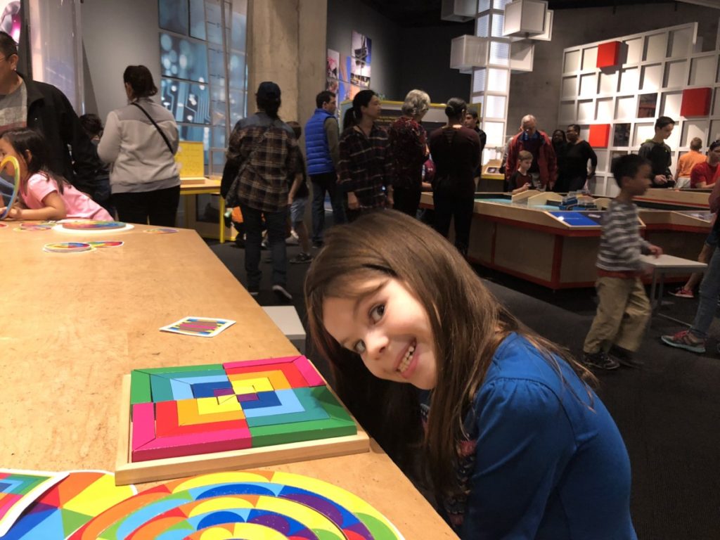 a girl smiles making Pattern blocks in STEM room Perot Musuem