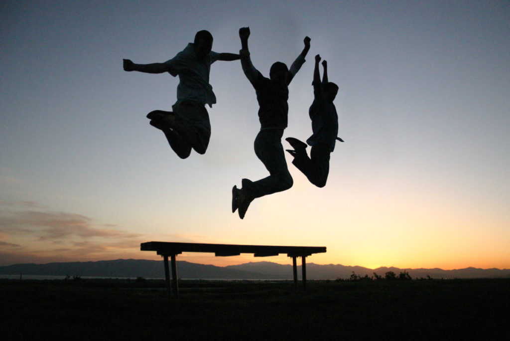 3 silhouette jumping in front of a sunset midair