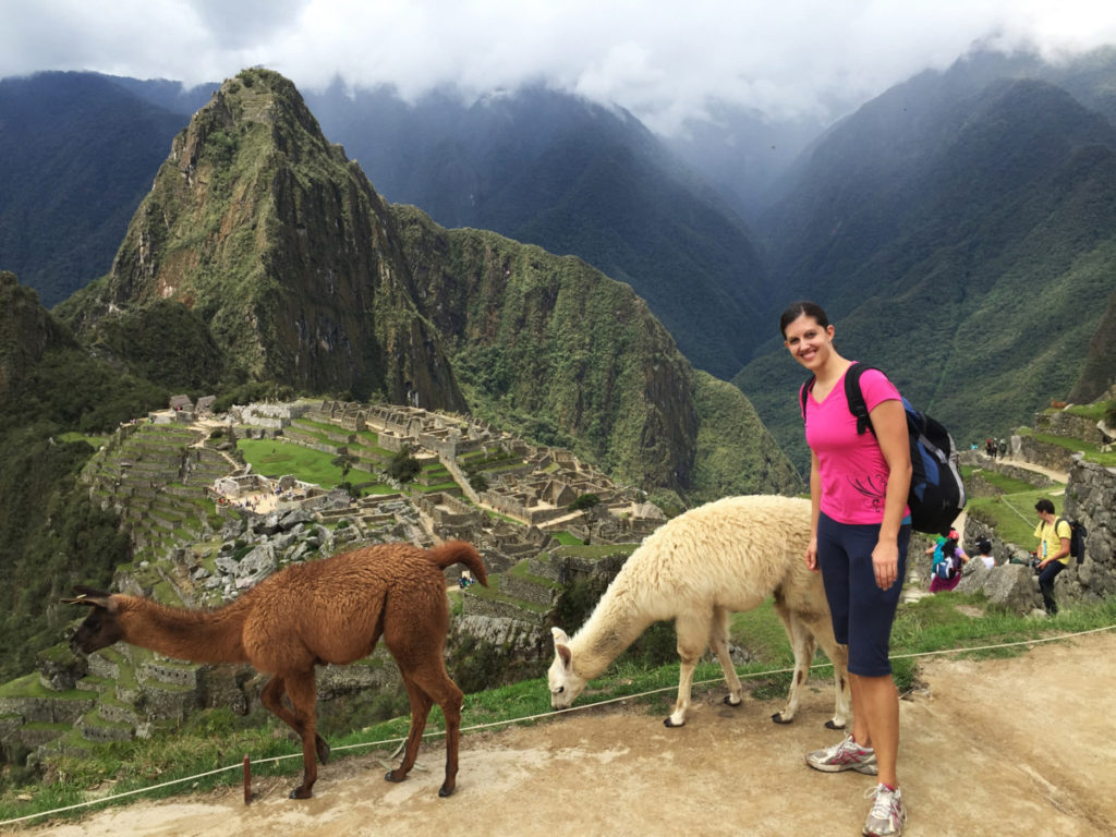 A woman stands with 2 llamas overlooking Machu PIcchu, peru