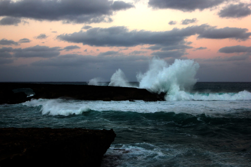 A giant wave crashes at La'ie Point in Oahu, Hawaii during a pink sunset