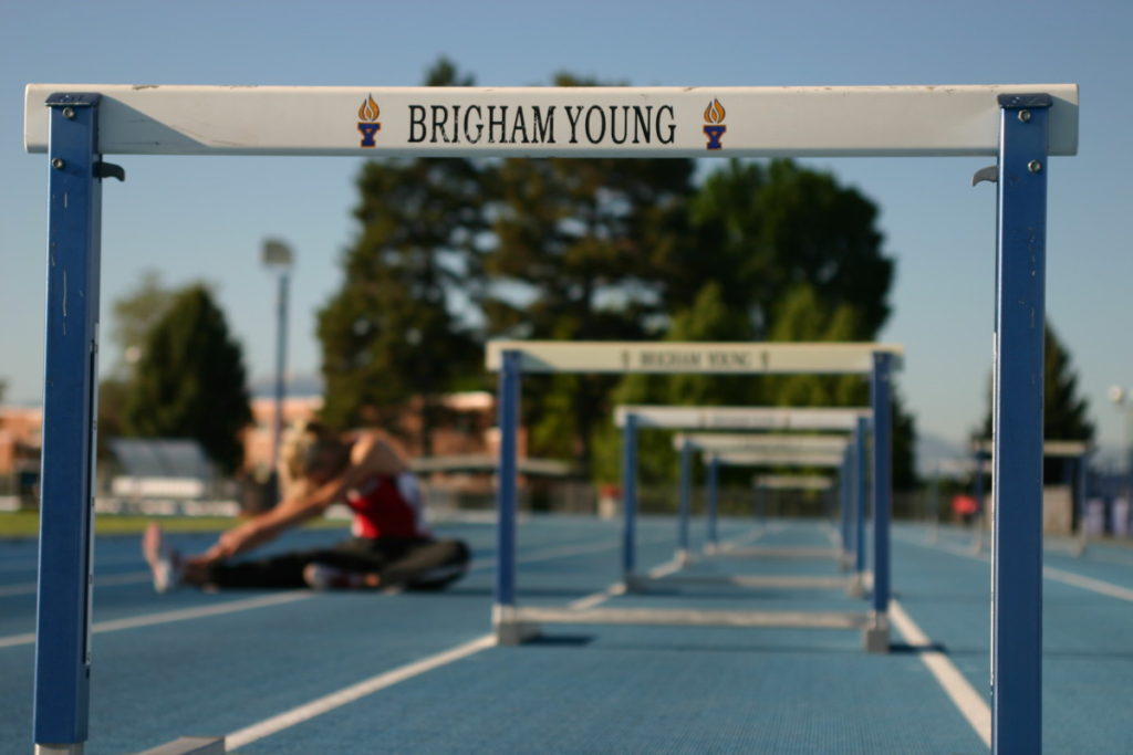 a runner stretches on a track with hurdles set up at Brigham Young University
