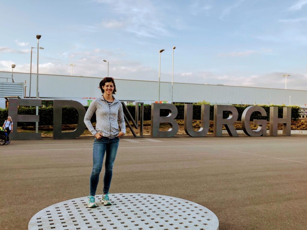 a Woman stands in front of Edinburgh Airport sign