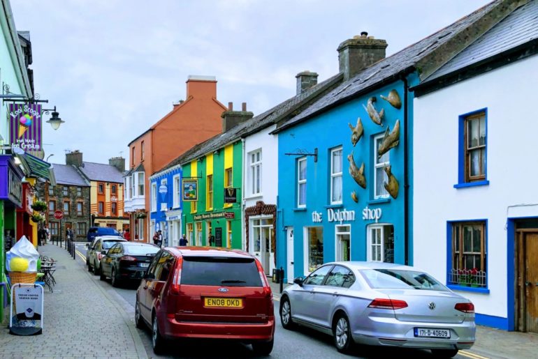 A small car driving in Ireland through a narrow road with parked cars in Dingle