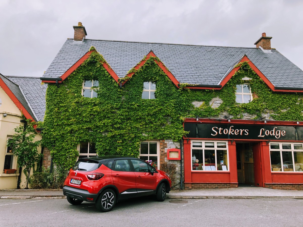 A small red car driving in Ireland in front of Stokers lodge in Tralee, Ireland.