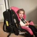 Baby strapped into a car seat is attached to luggage for travels