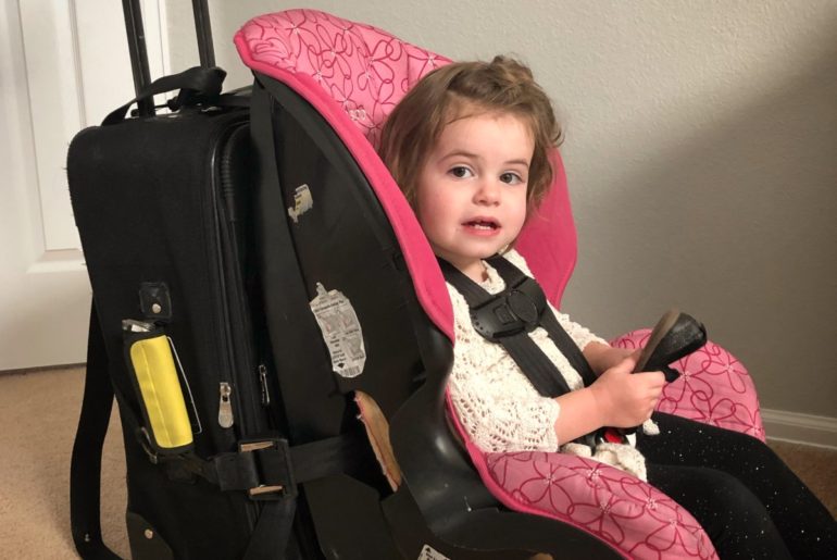 Baby strapped into a car seat is attached to luggage for travels