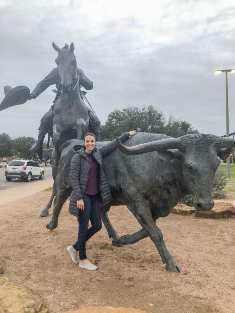 a Woman stands at the Longhorn and cowboy Sculpture at Waco Suspension Bridge