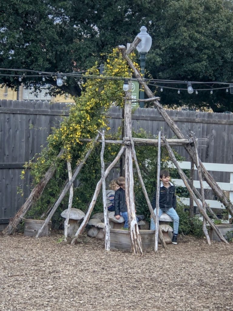 kids sitting under a wood teepee in the garden area ath Magnolia Market in Waco