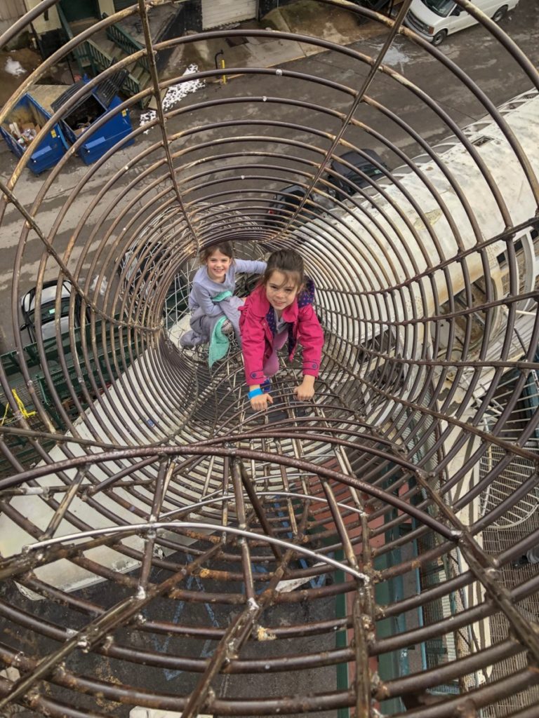 2 girls climb a metal structure above an airplane perched outside the City Museum
