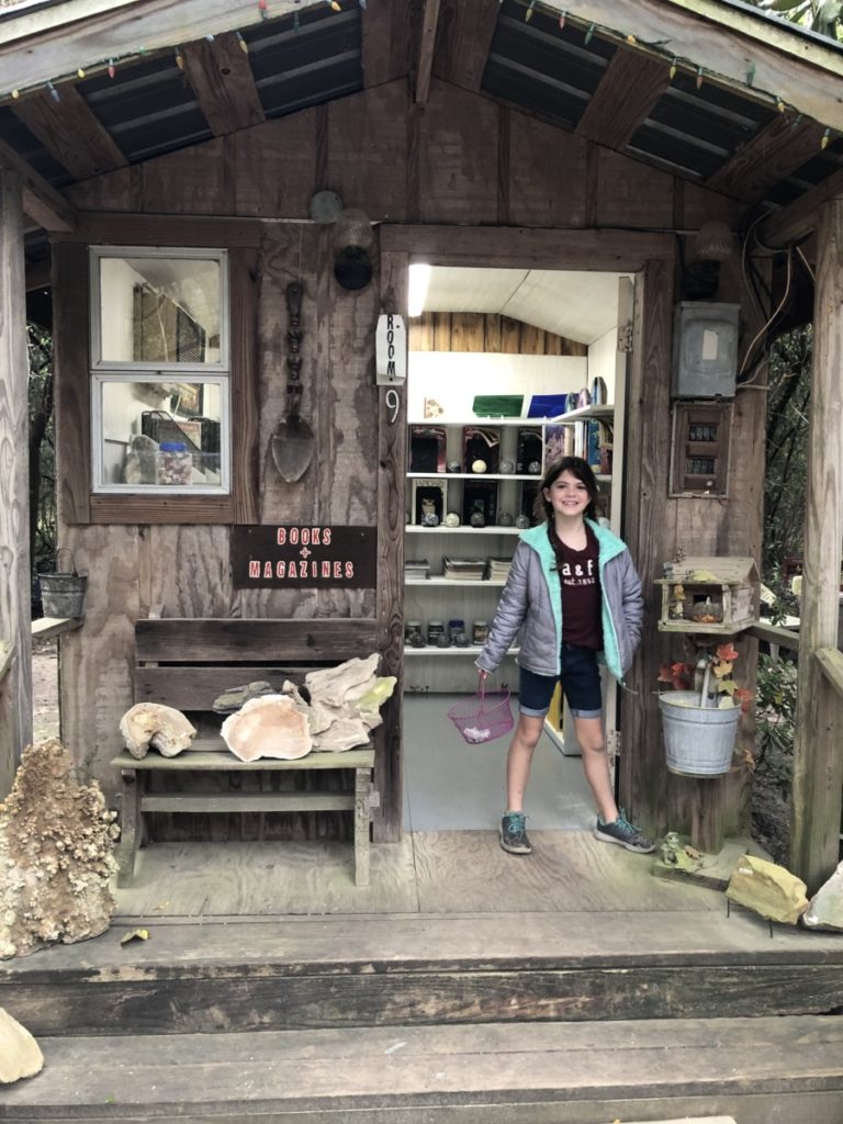 a Girl stand with a bucket of rocks in front of Johnson's rock shop cabin at Lake Livingston
