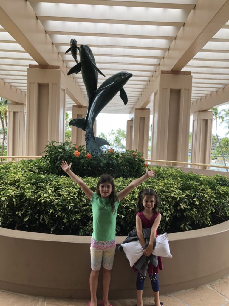 two girls stand in front of the Dolphins statue at Hilton Waikoloa