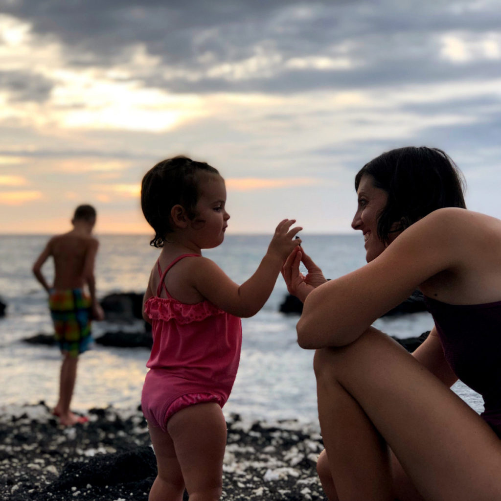 A mom and toddler explore the rocks at Hilton Waikoloa on the black and white rocky shore.