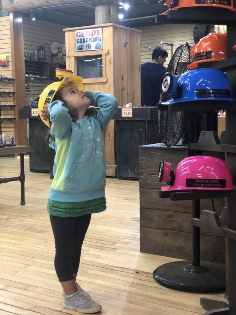 A little girl tries on a cave explorers helmet in a gift shop