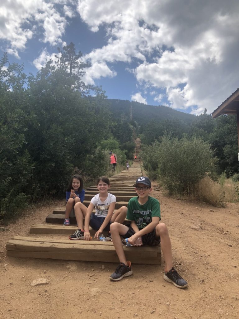 3 kids sit at the bottom of Manitou Springs Incline Hike in Colorado Springs with kids