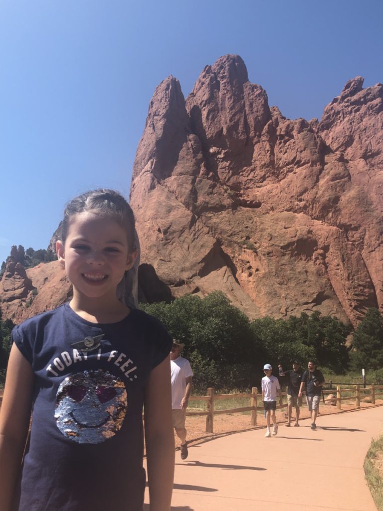 A young girl smiles in front of the red rocks at Garden of the Gods