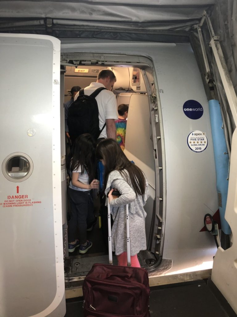 A Dad boarding an airplane with his daughter dragging a suitcase