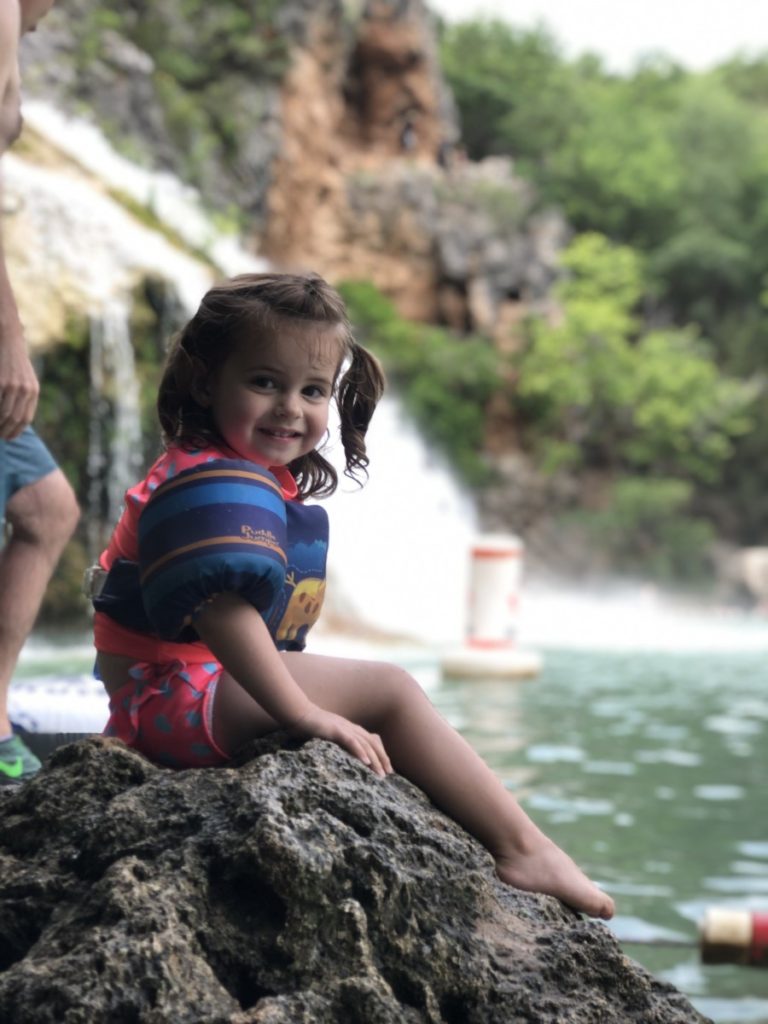 A Toddler smiles in front of Turner Falls