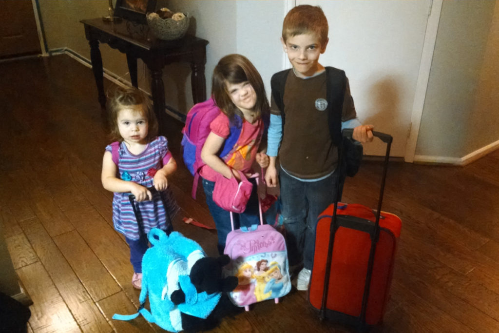 3 kids pulling small luggage with backpacks on