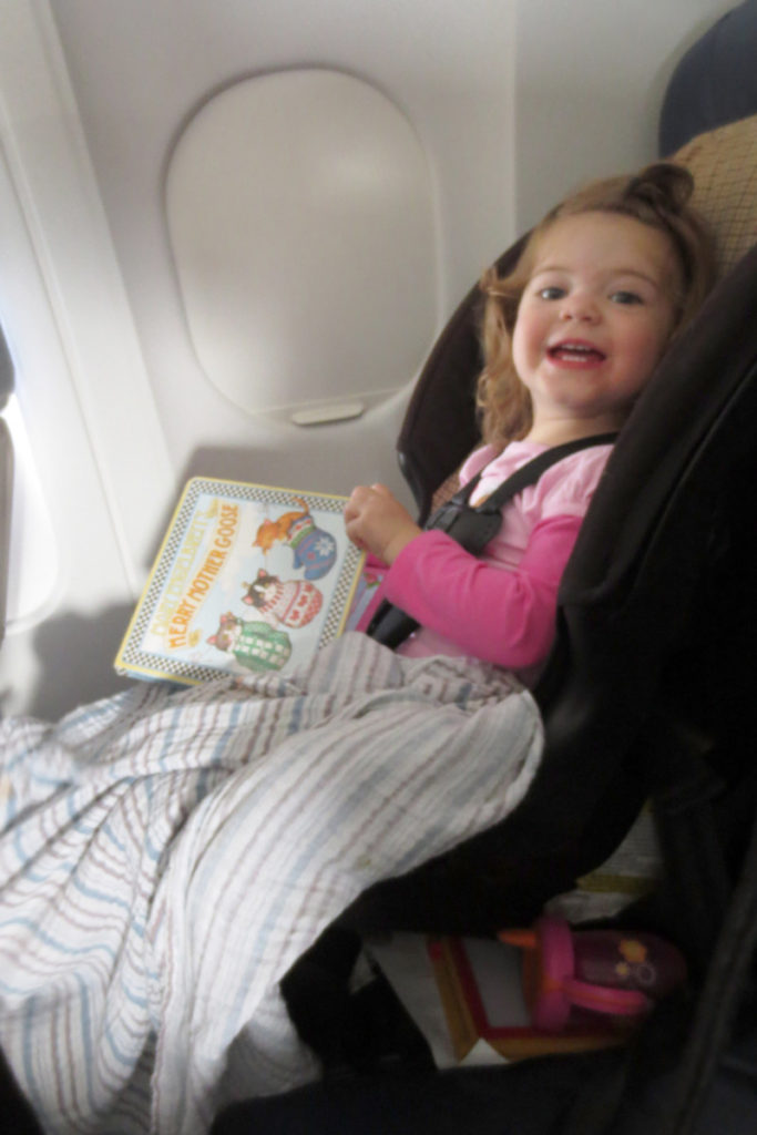 Toddler reading a board book in a car seat on the flight